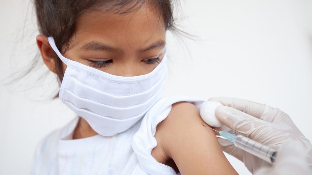 Doctor injecting vaccination on asian child girl arm. The child girl wearing protection mask for protect air smog pollution with PM 2.5 and Covid-19 virus